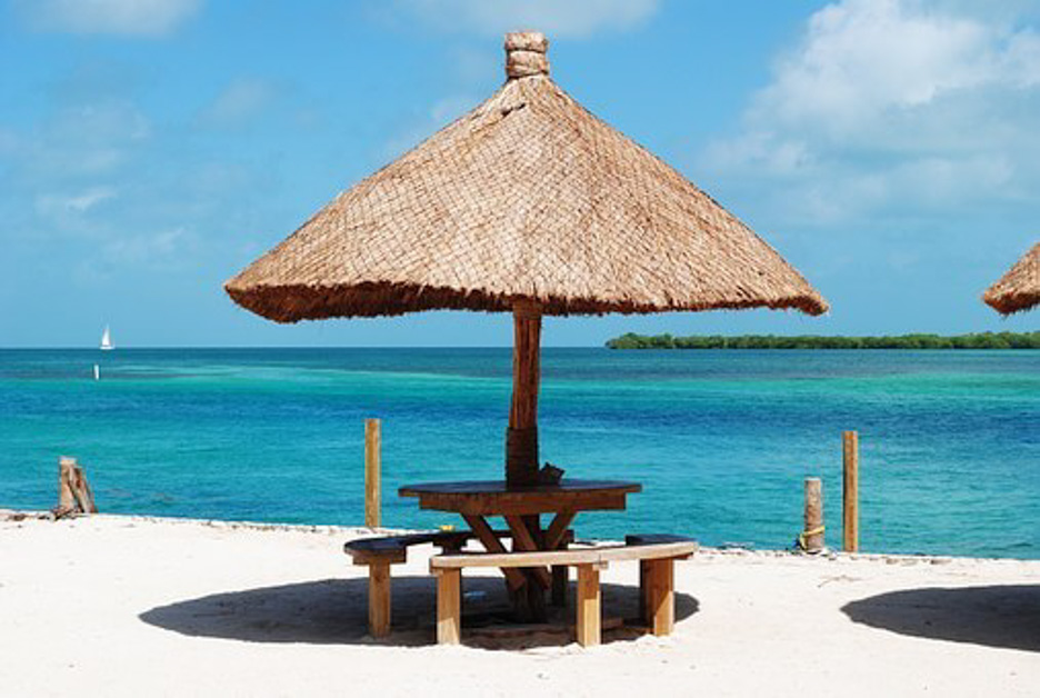 straw umbrella and wooden chairs on a beach in Belize